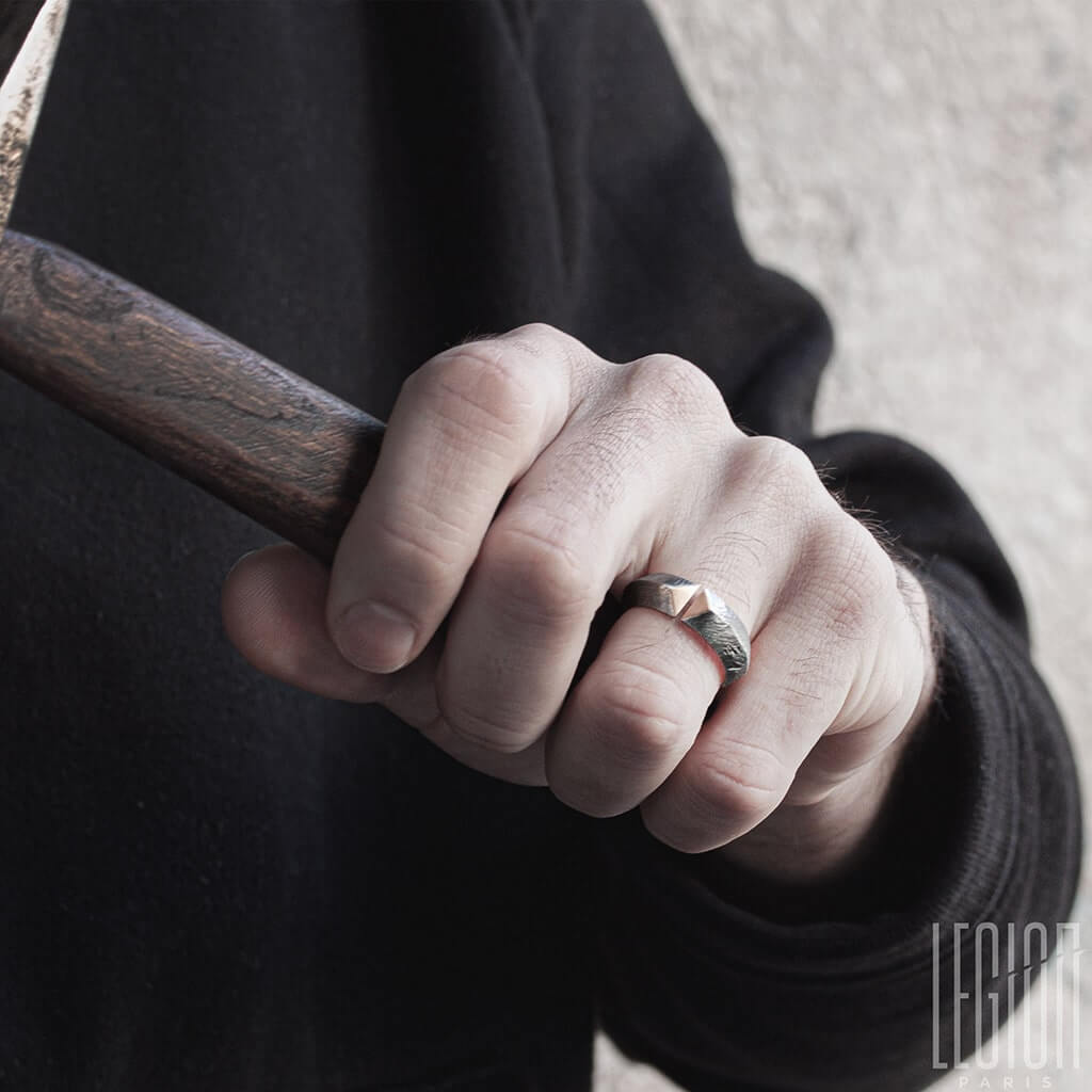 main d'homme habillé en noir portant une bague ouverte en argent noir et or rouge