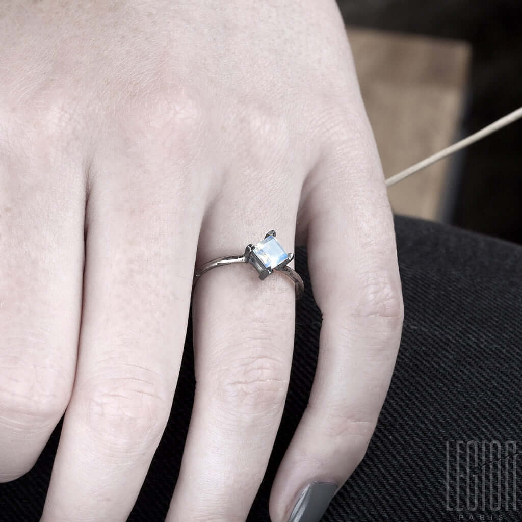 main de femme portant une bague en or blanc et pierre de lune carrée