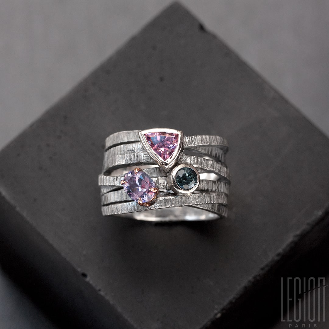 Chevalière large avec des brindilles d'argent noir texturées et entrecroisées et 3 pierres sur le dessus. Un spinelle triangle rose, une tourmaline bleue ronde , les deux sont serties clos avec de l'or blanc, et une tourmaline mauve ovale sertie en griffes dans un châton en or rouge