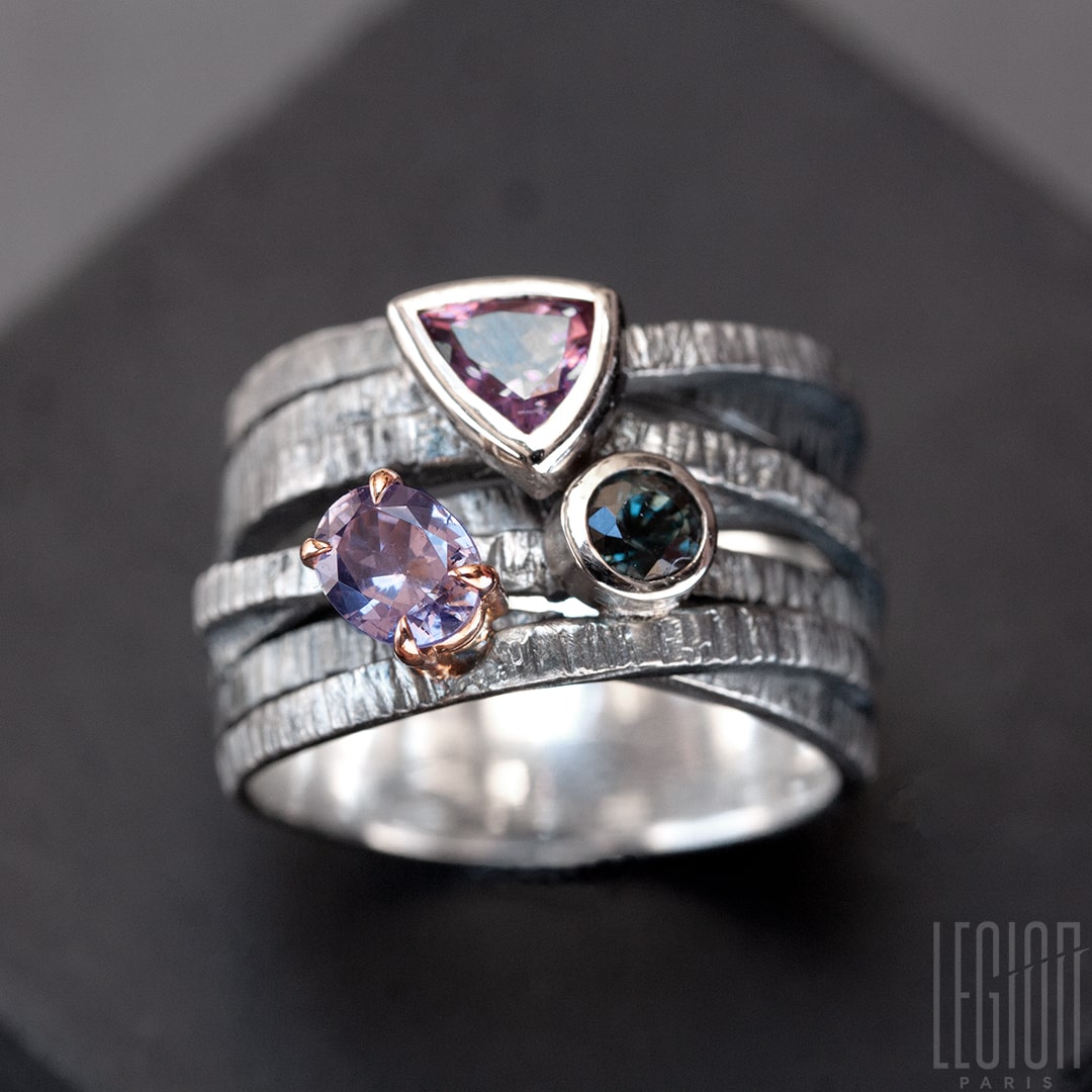 Chevalière large avec des brindilles d'argent noir texturées et entrecroisées et 3 pierres sur le dessus. Un spinelle triangle rose, une tourmaline bleue ronde , les deux sont serties clos avec de l'or blanc, et une tourmaline mauve ovale sertie en griffes dans un châton en or rouge
