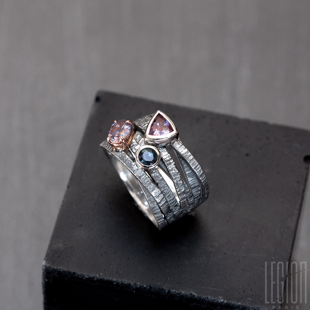 Chevalière large avec des brindilles d'argent noir texturées et entrecroisées et 3 pierres sur le dessus. Un spinelle triangle rose, une tourmaline bleue ronde , les deux sont serties clos avec de l'or blanc, et une tourmaline mauve ovale sertie en griffes dans un châton en or rouge