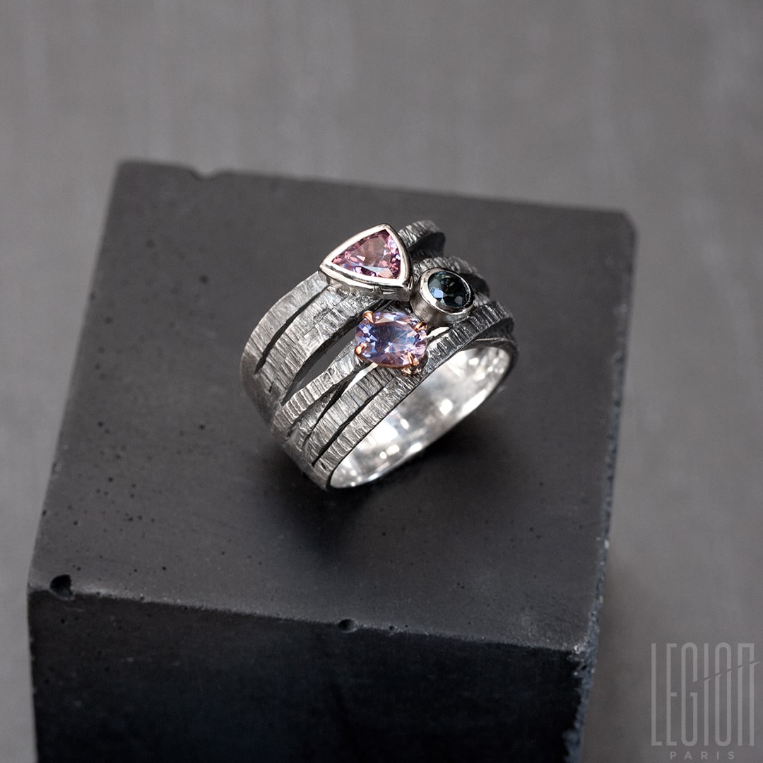 Chevalière large avec des brindilles d'argent noir texturées et entrecroisées et 3 pierres sur le dessus. Un spinelle triangle rose, une tourmaline bleue ronde , les deux sont serties clos avec de l'or blanc, et une tourmaline mauve ovale sertie en griffes dans un châton en or rouge