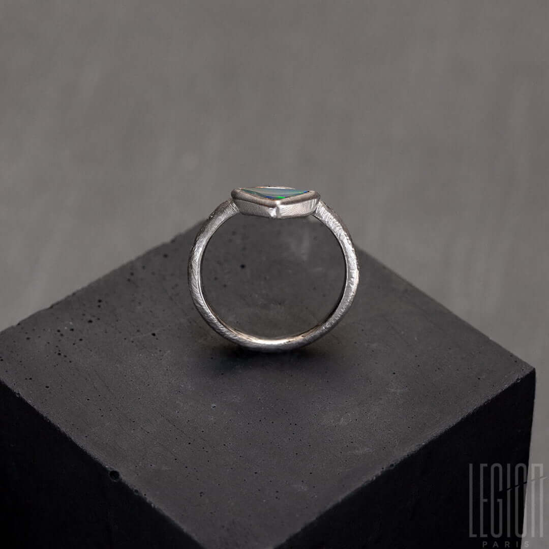vue de côté d'un Anneau de bague en or blanc texturé avec des diamants gris placés aléatoirement et une opale noire triangle avec des feux vert et orange