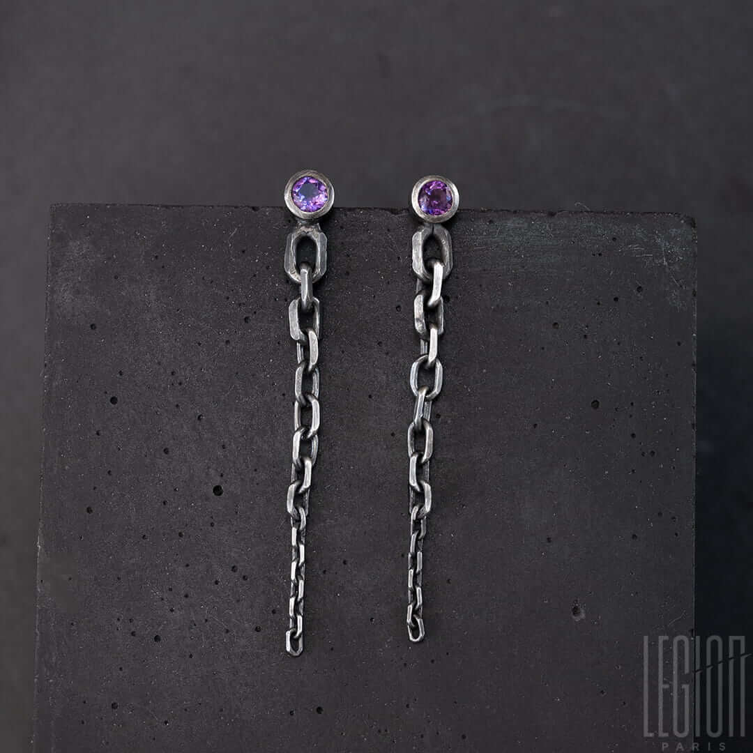 boucles d'oreilles en argent noir. chaque boucle à une pierre ronde violette sertie en clos. De cette pierre part une chute de chaine en maille forcat de la plus grosse à la plus fine