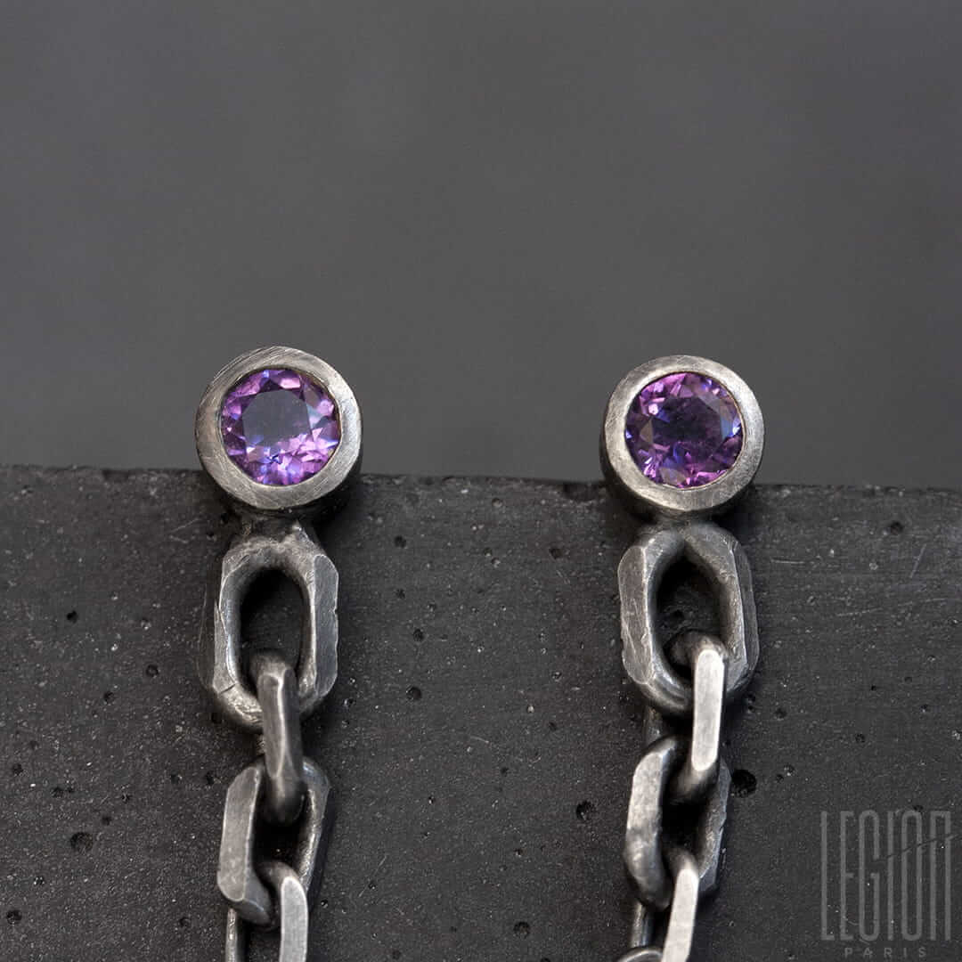 gros plan sur deux amethystes violettes rondes serties en clos avec une chute de chaine en argent noir
