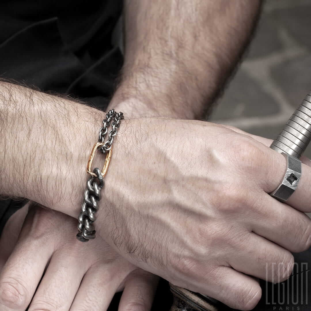 poignet d'homme portant un bracelet en argent noir et or rouge en chaine gourmette et une bague chevaliere en argent noir