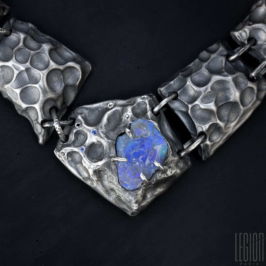 Gros plan sur une tuile centrale du collier en argent noir avec une opale noire brut sertie avec 4 griffes en argent et des saphirs et diamants eparpillés autour.