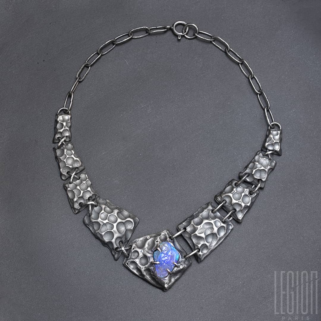 un collier plastron en argent noir fait de différentes tuiles texturées en argent noir avec au centre un opale noire brute