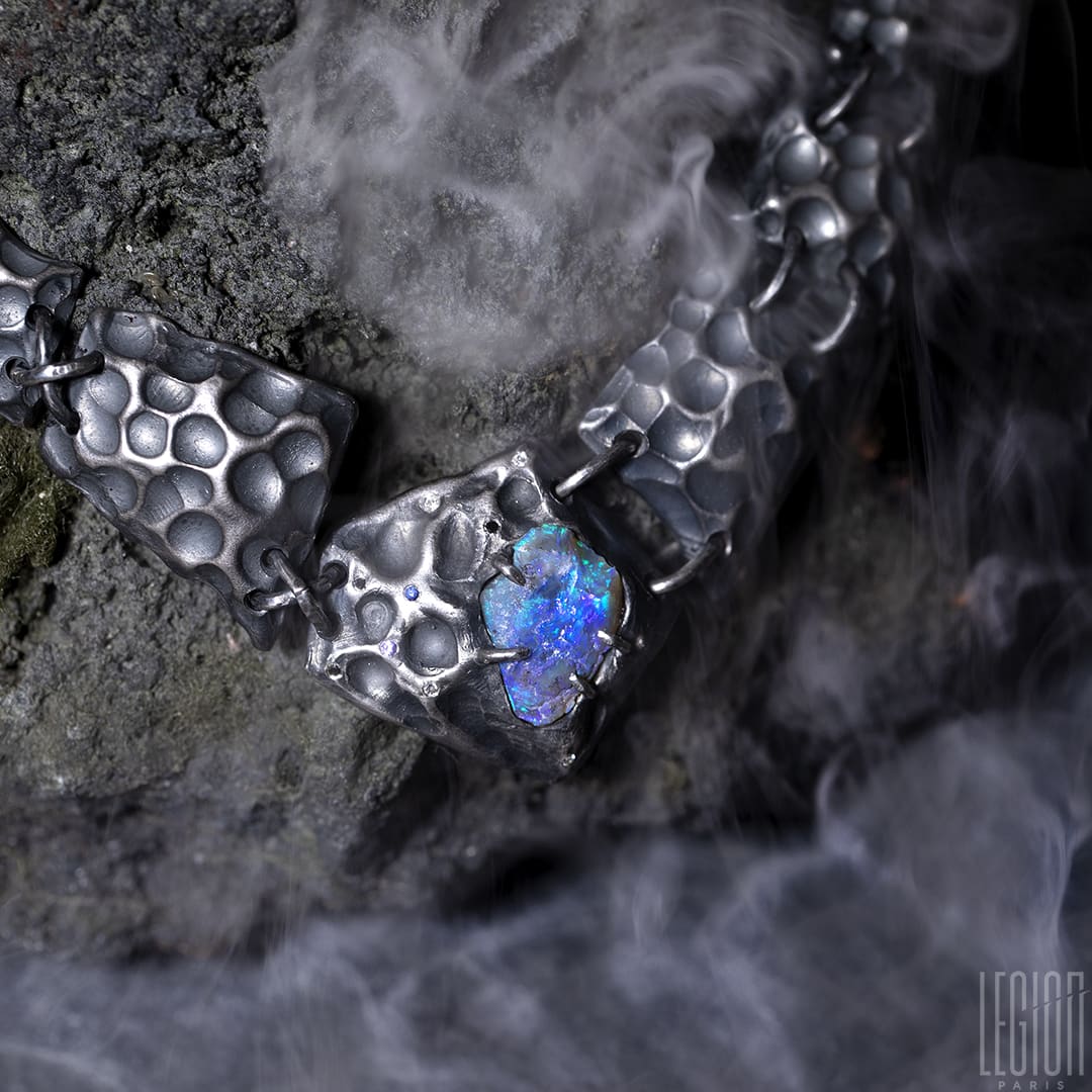 un collier plastron en argent noir fait de différentes tuiles texturées en argent noir avec au centre un opale noire brute