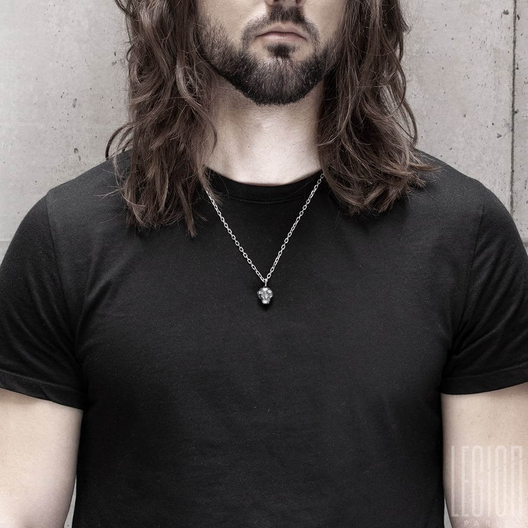 homme aux cheveux longs noir portant un tee shirt noir avec un pendentif en forme de tête d'ours en argent noir