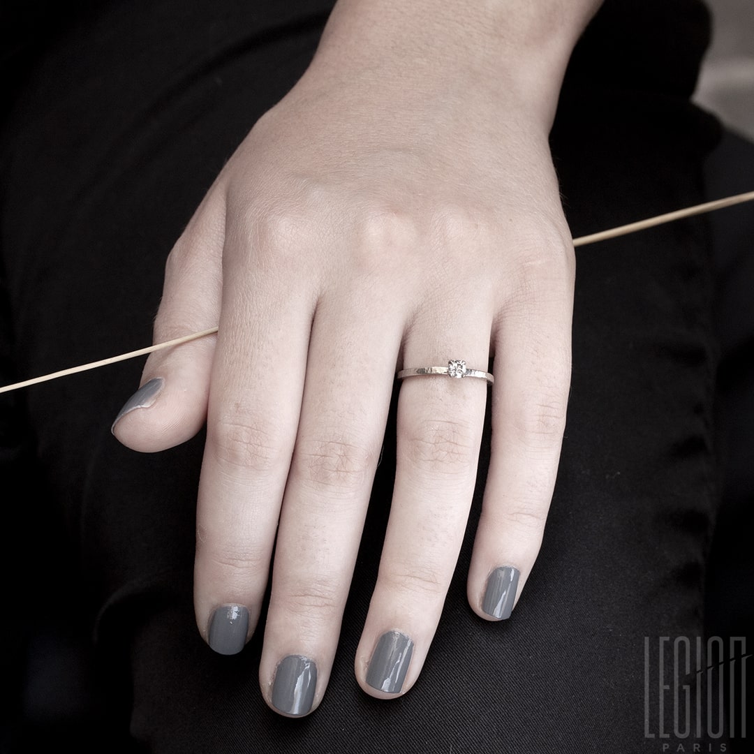 Main de femme portant un Bague solitaire en or blanc legerement martelé avec un diamant gris rond