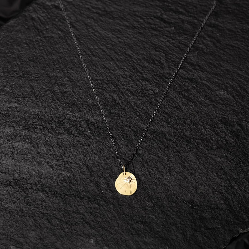 yellow gold medal with a champagne diamond on a black silver chain