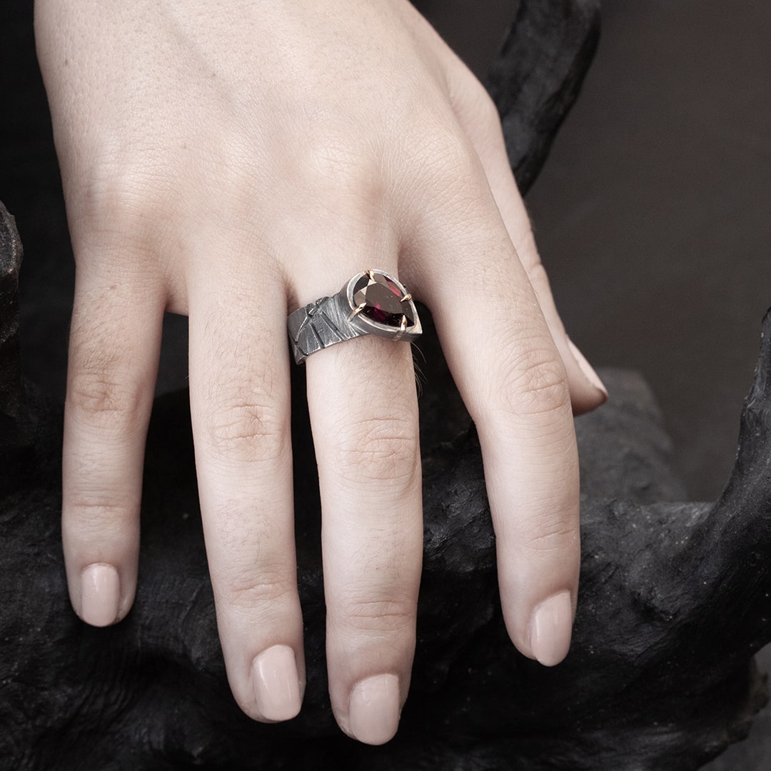 main de femme portant une bague large originale en argent et or jaune avec un grenat rouge