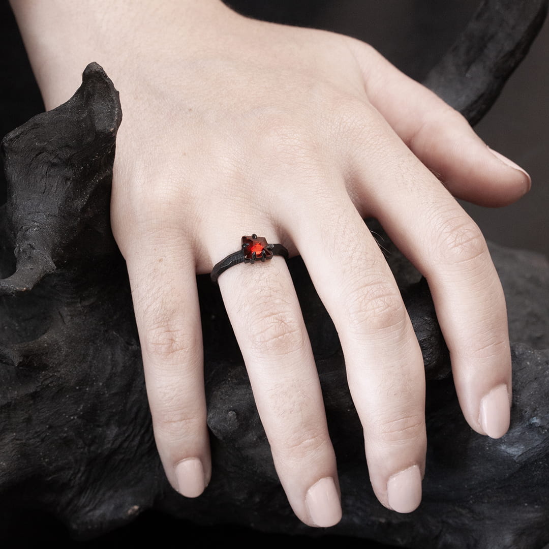 main de femme portant une bague de fiançailles en or noir avec un grenat rouge