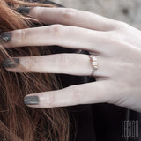 main de femme rousse avec des ongles gris portant une bague fine en or blanc et rouge et diamants