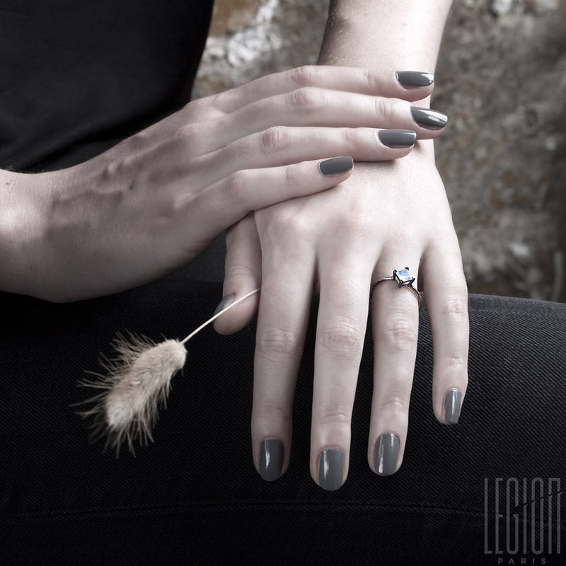 mains de femme avec des ongles gris portant une bague avec une pierre carrée blanche