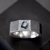anneau facetté, texturé comme un ecrou en argent noir avec une pierre bleue carrée sertie dans le métal