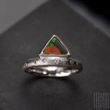 Annreu de bague en or blanc texturé avec des diamants gris placés aléatoirement et une opale noire triangle avec des feux vert et orange