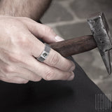 main d'homme portant un anneau facetté, texturé comme un ecrou en argent noir avec une pierre bleue carrée sertie dans le métal