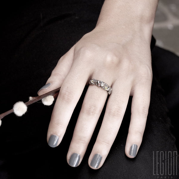 main de femme avec des ongles gris portant un anneau en or blanc texturé avec des petites pierres brillantes eparpillées sur le dessus.