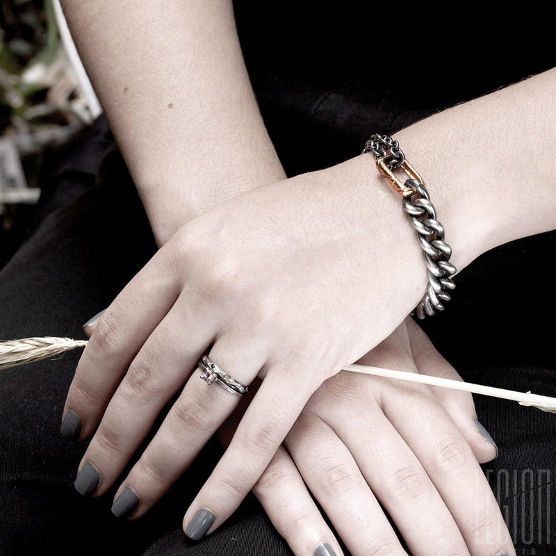 poignet de femme portant un bracelet en argent noir et or rouge en chaine gourmette et une alliance en or blanc texturée et un solitaire en or blanc avec un diamant gris