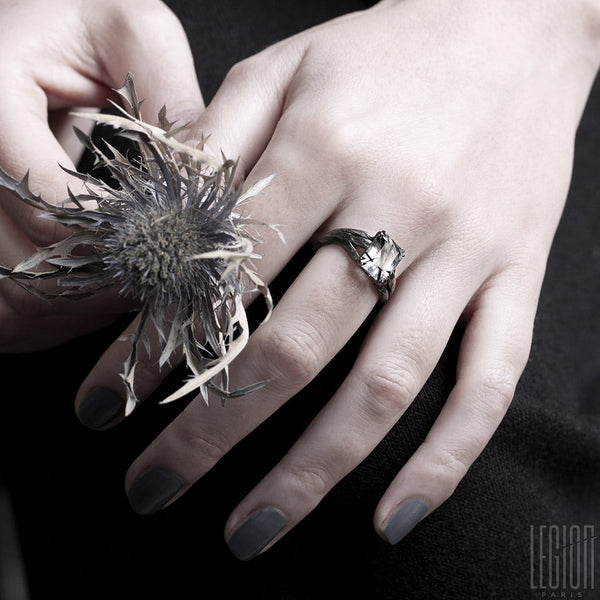 mains de femme portant une bague de fiançailles en or noir avec un quartz rutile