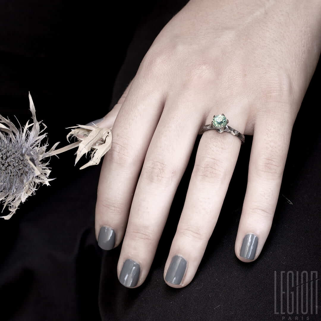 main de femme portant une bague solitaire en or blanc texturé avec une pierre bleue claire aigue marine