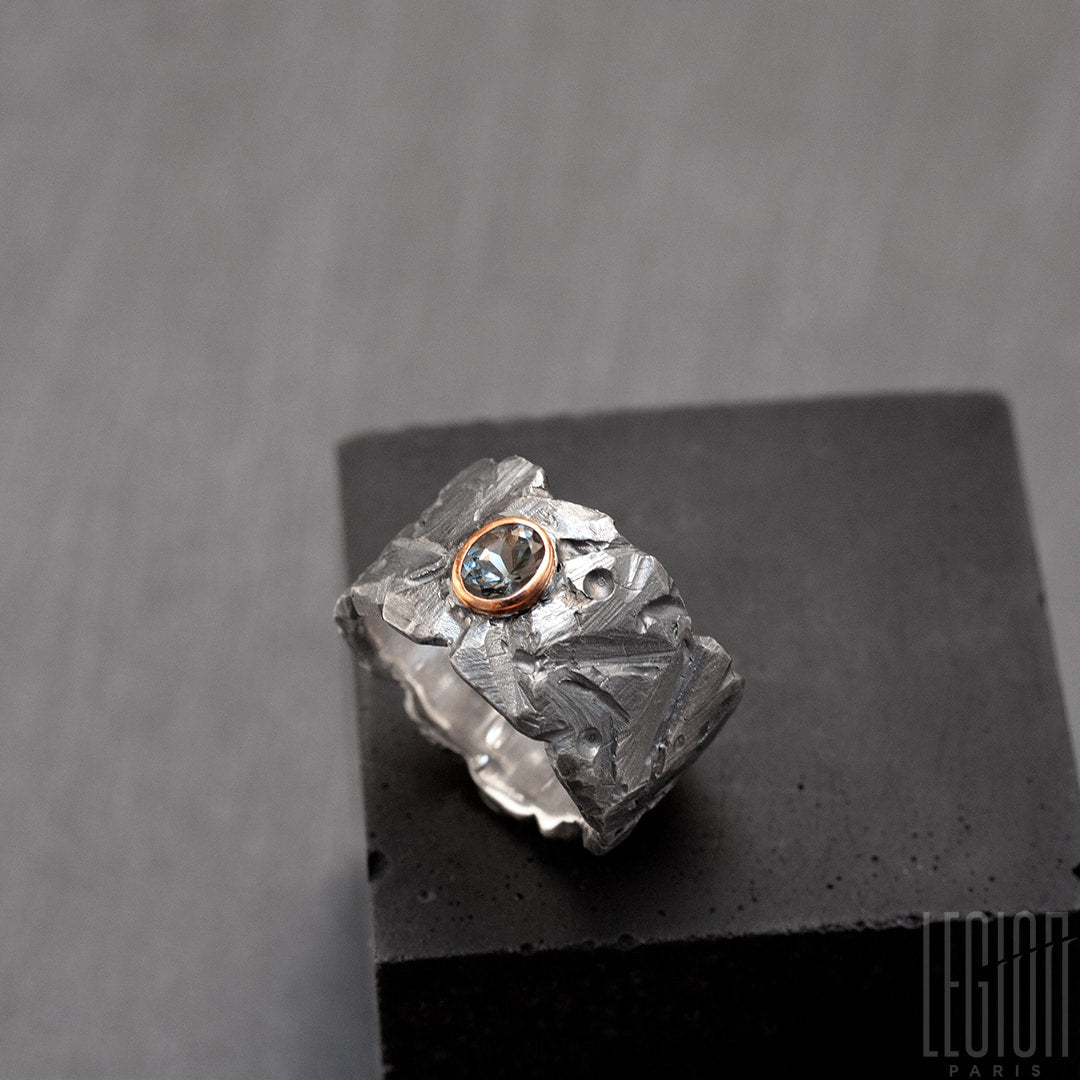 Vue latérale d'une bague très large en argent noir texturé avec une pierre ovale, un spinelle gris vert, serti en clos en or rouge. 