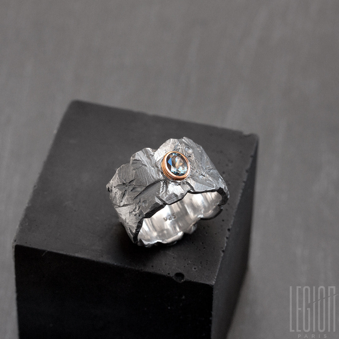 Vue latérale d'une bague très large en argent noir texturé avec une pierre ovale, un spinelle gris vert, serti en clos en or rouge. 