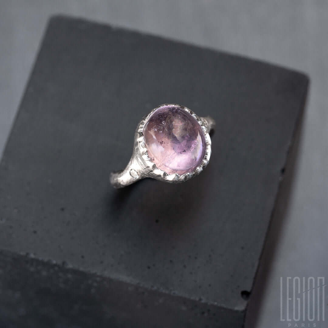 vue de côté d'une bague chevaliére en or blanc texturé avec un diamant gris sur le côté et une grosse pierre centrale mauve translucide et ovale