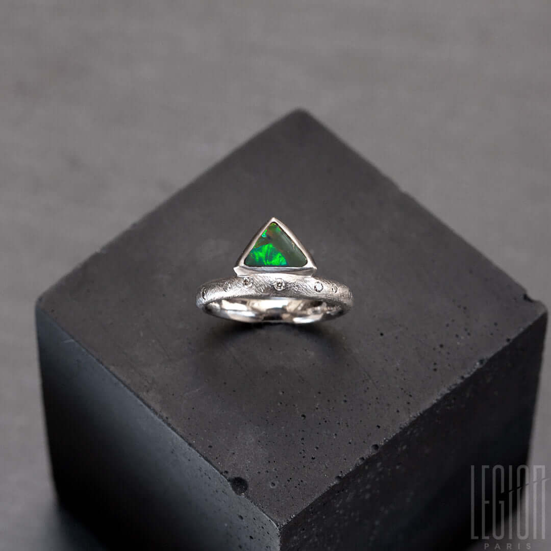 Annreu de bague en or blanc texturé avec des diamants gris placés aléatoirement et une opale noire triangle avec des feux vert et orange
