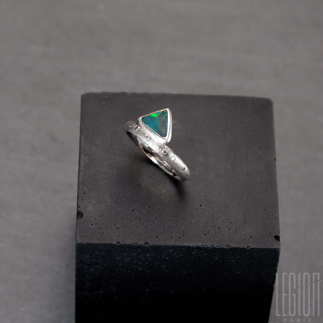 Bague en or blanc texturé avec des diamants gris placés aléatoirement et une opale noire triangle avec des feux vert et orange