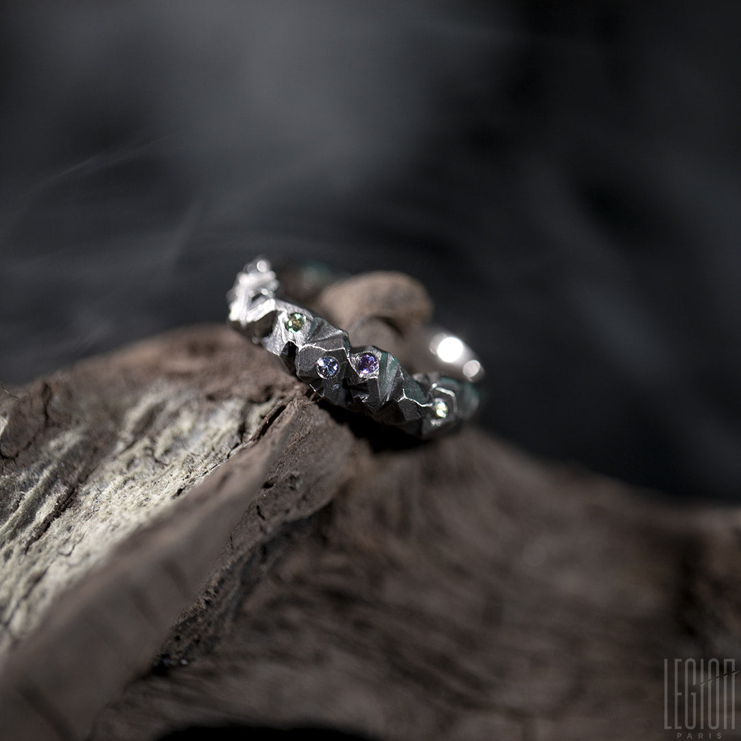 bague en or blanc posée sur une racine. Sur la bague des petits brillants de différentes couleurs sont serties et éparpillées dessus. 