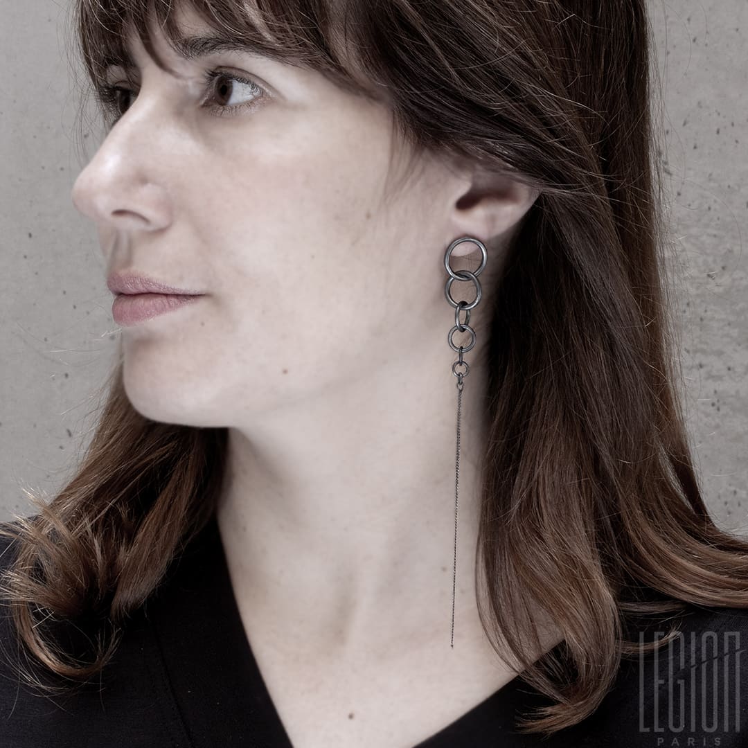 femme rousse portant une boucle d'oreille en argent noir très longue faite d'anneaux de différentes tailles et se terminant par une chaine longue gourmette très légère. 