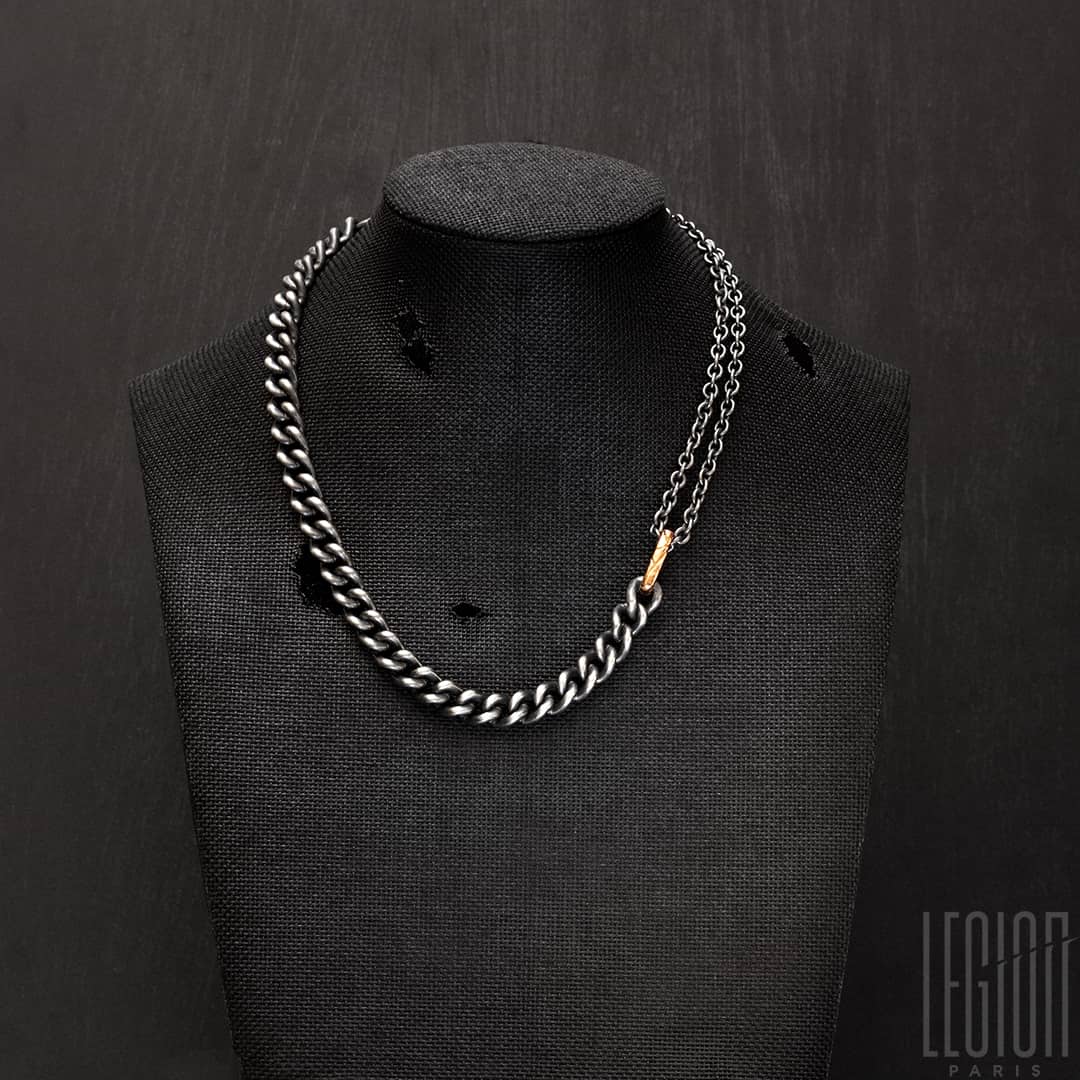 collier sur un buste noir en tissu avec un collier en chaines en argent noir et or rouge avec différentes chaines de différentes tailles 