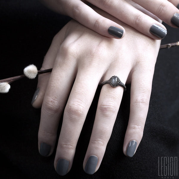 mains de femmes portant une bague en argent noir avec une pierre de lune grise