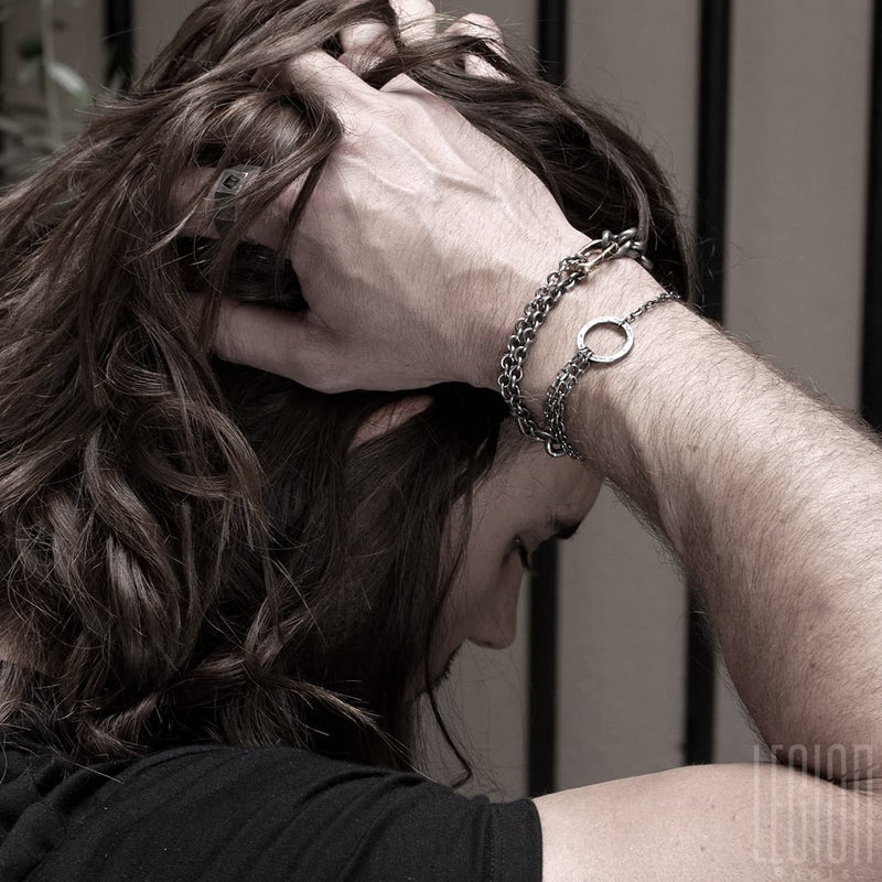 homme aux cheveux longs portant un tee shirt avec à son poignet deux bracelets en argent noir en chaine