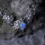 un collier plastron en argent noir fait de différentes tuiles texturées en argent noir avec au centre un opale noire brute
